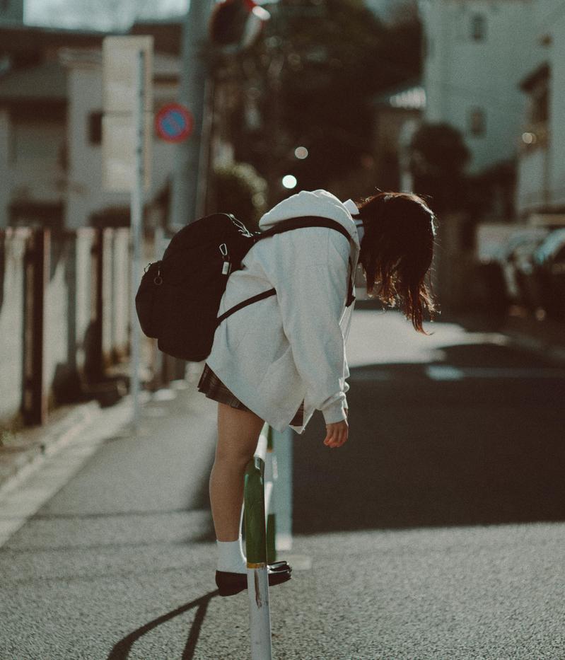 白いパーカーにリュックを背負い通学路で前屈みになる女子高生の後ろ姿
