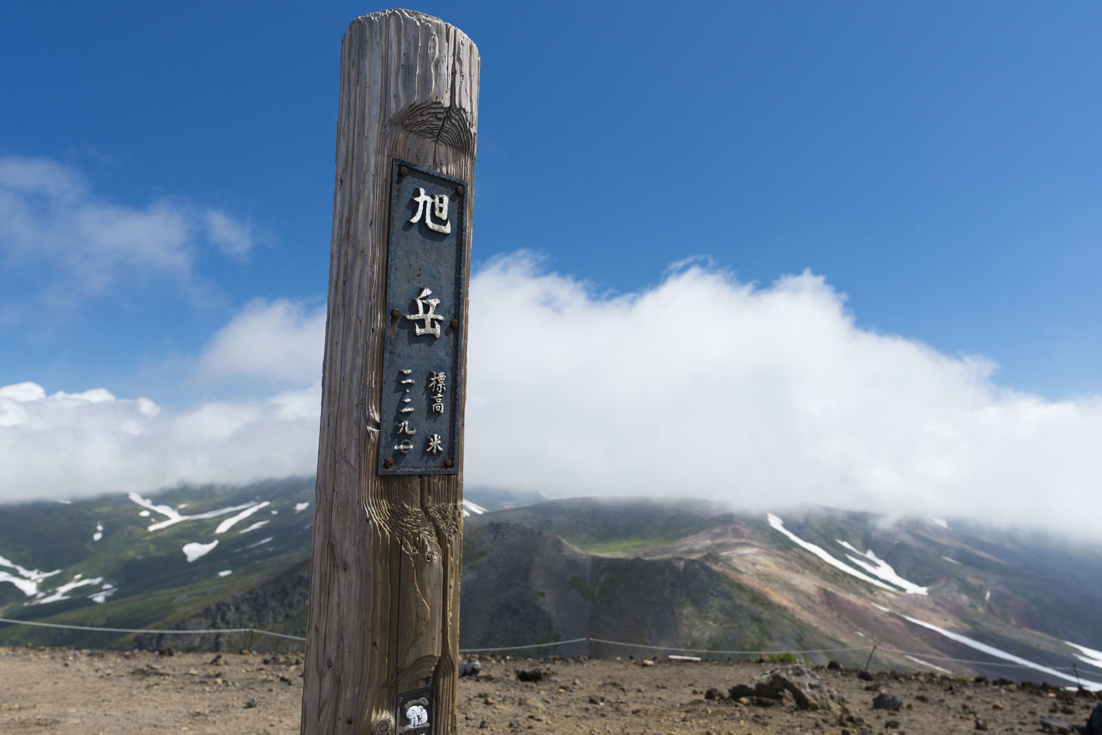 青空と雲を背景に旭岳山頂に立つ日本百名山の木製標識