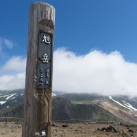 背景に雲が流れる旭岳山頂の木碑｜日本百名山の写真