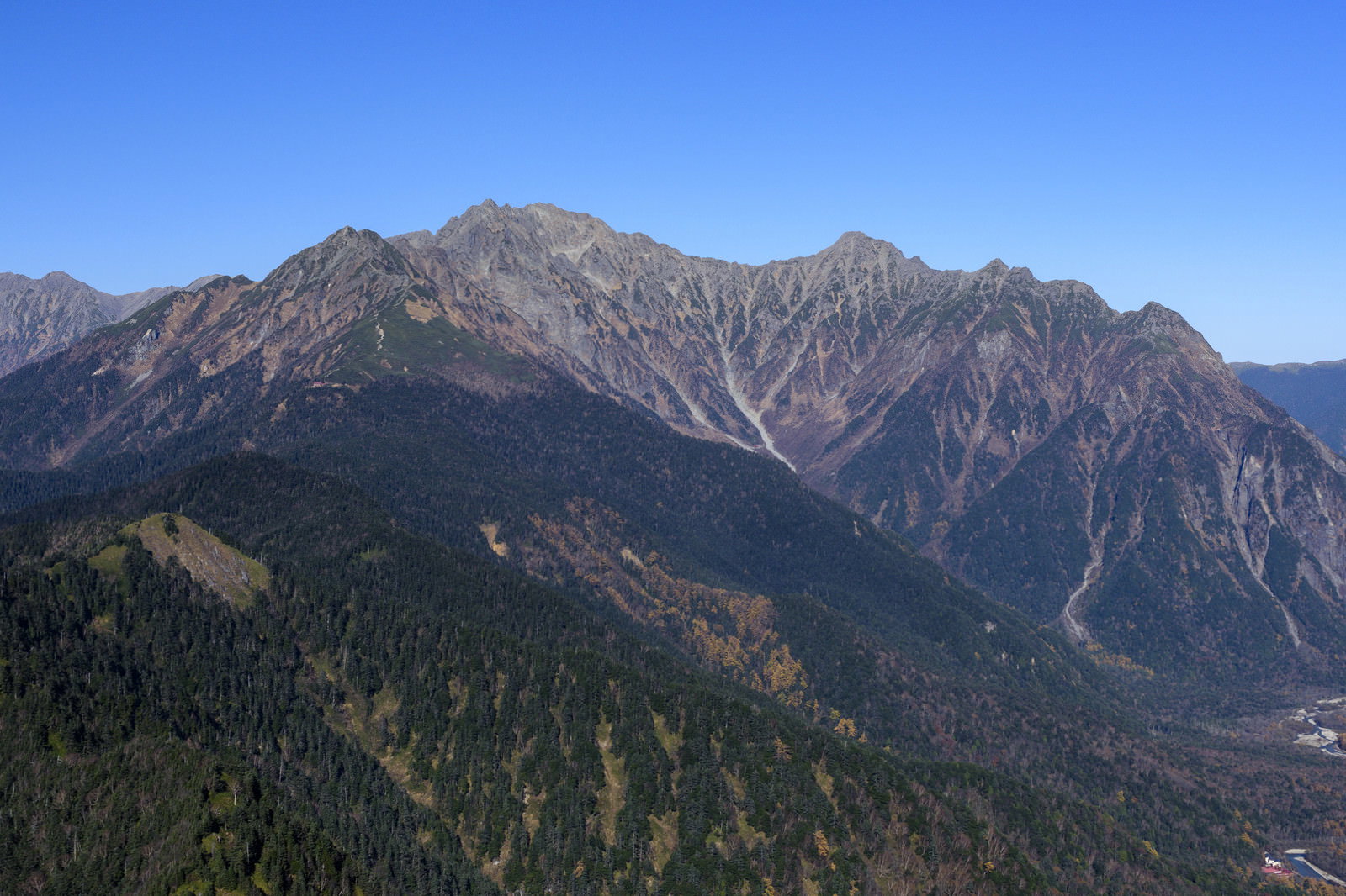 青空をバックに穂高岳の険しい山並みと緑の森林が広がる山岳風景