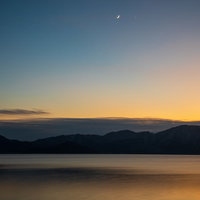 夕焼けに染まる田沢湖の湖面と遠くの山並みのシルエットの写真