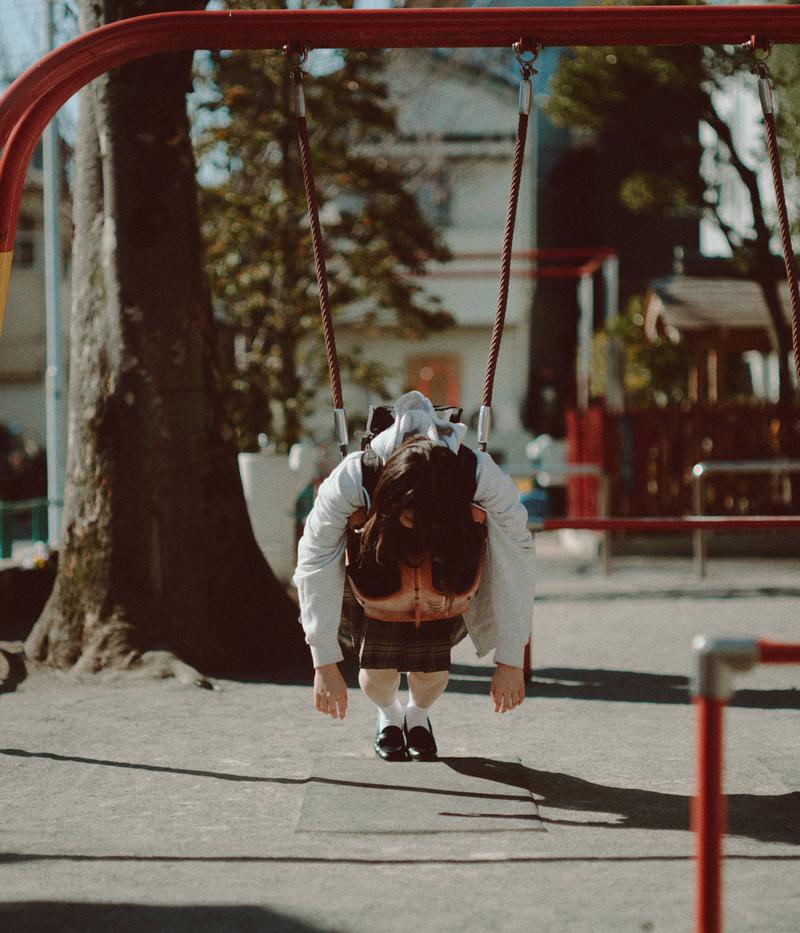 公園のブランコに乗ってうなだれている女子高生