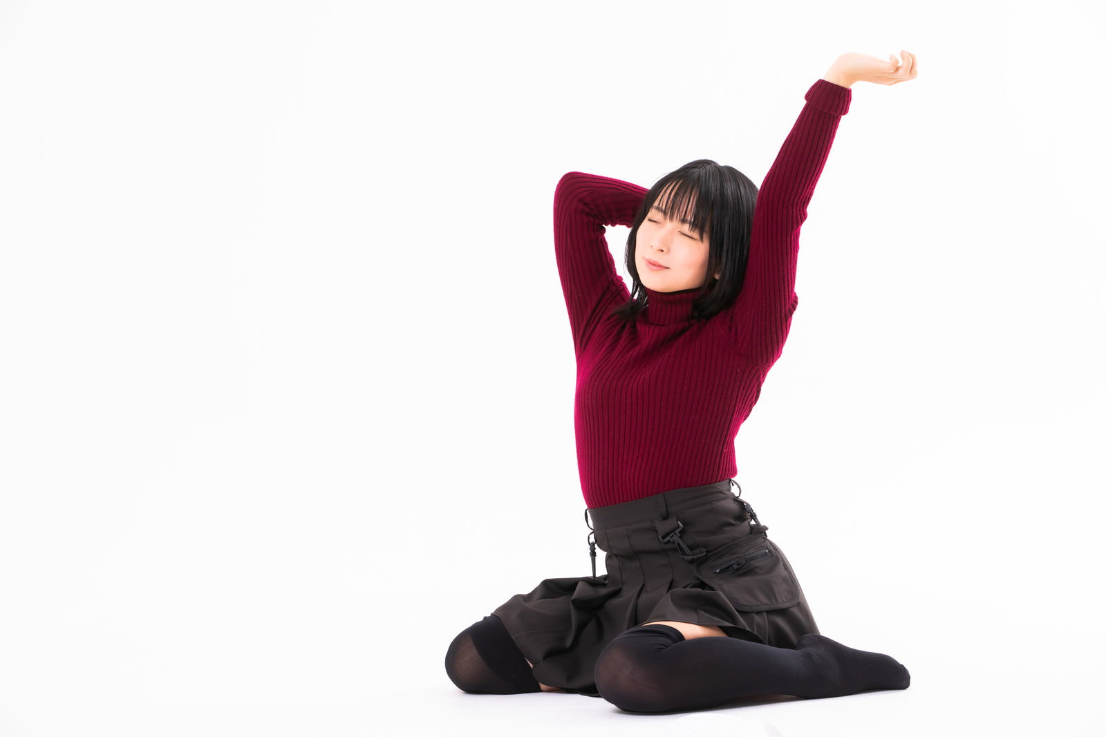 赤紫色のニットを着た女性が座りながら両手を上に伸ばしてあくびをしている［モデル：にゃるる］
