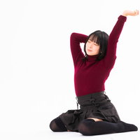 赤紫色のニットを着て座りながら大きく伸びをする女性の写真