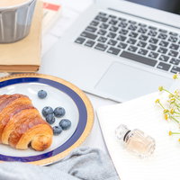 デスク上に置かれたクロワッサンとコーヒーの朝食の写真
