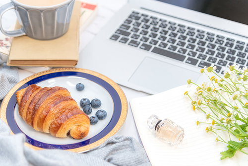 デスク上に置かれたクロワッサンとコーヒーの朝食