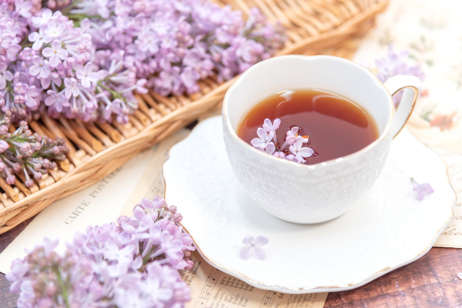 木製トレーの上に置かれた紅茶のティーカップと籠に入ったライラックの花