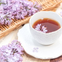 木製トレーにのせたライラックの浮かぶ紅茶のティーカップの写真