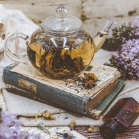 ハーブティーと洋書、紫色の小花が並ぶティータイムの写真