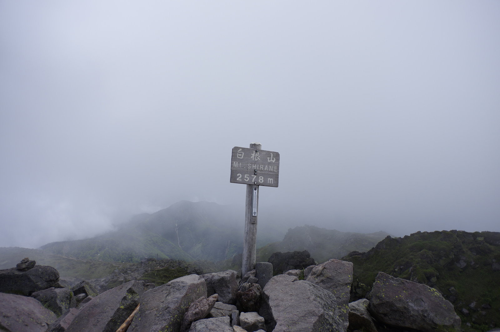 濃い霧に覆われた日光白根山山頂の木製指導標と岩場の風景