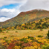 秋の紅葉に染まる栗駒山を上る登山客の写真