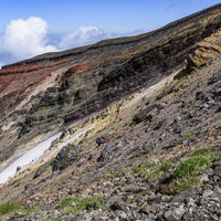 重なり合う地層が見える旭岳の爆裂火口の岩肌の写真
