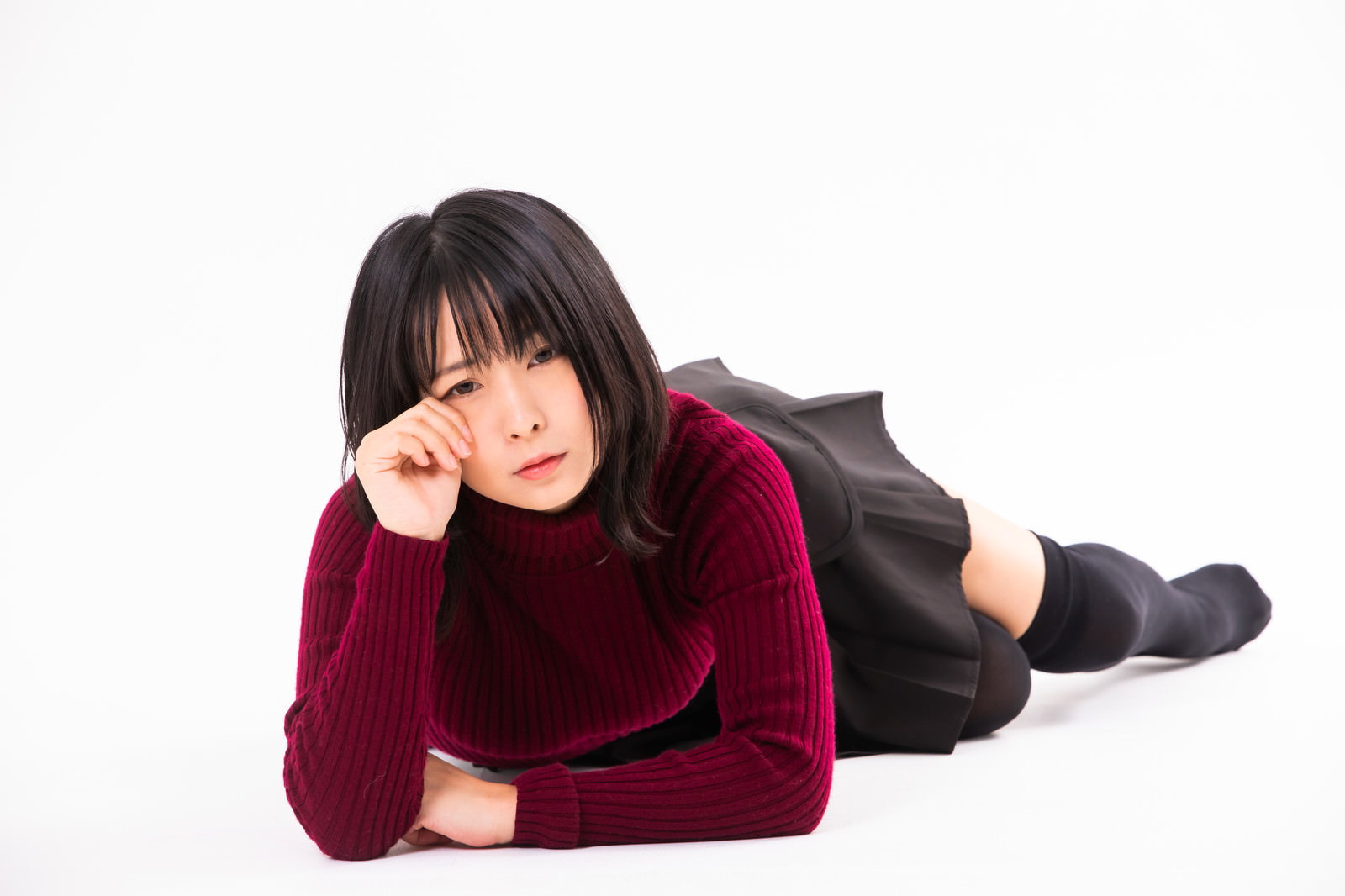 エンジ色のセーターを着た女性が床に横になって涙を流している［モデル：にゃるる］