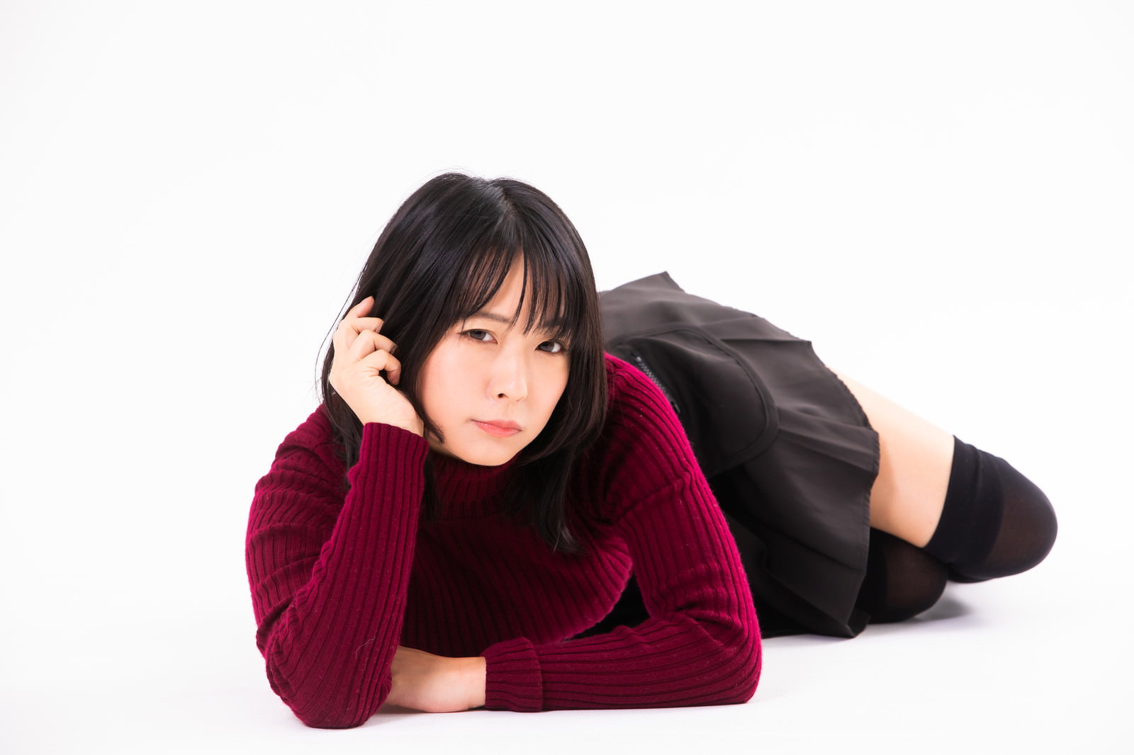 えんじ色のニットを着た女性が床に横たわり頬杖をついている［モデル：にゃるる］