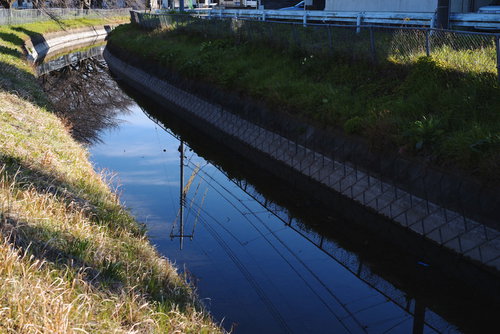 川の水面に映る電柱と青空、コンクリート水路の反射風景