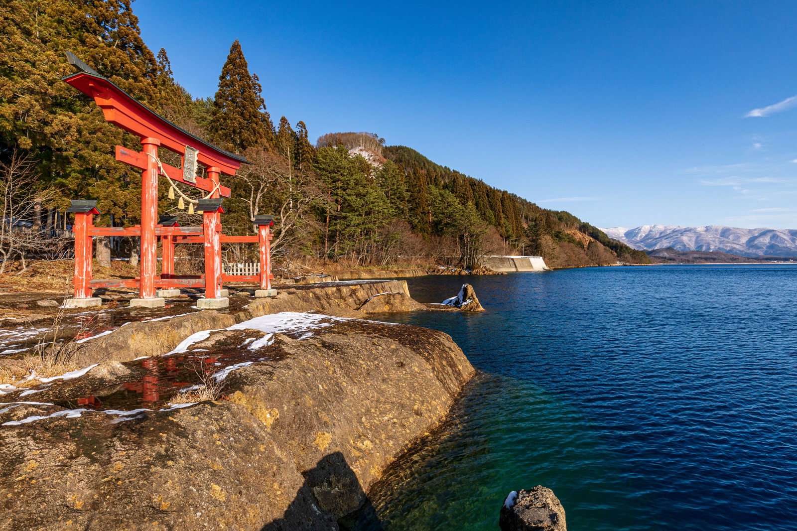 田沢湖畔に立つ御座石神社の朱色の鳥居と雪山