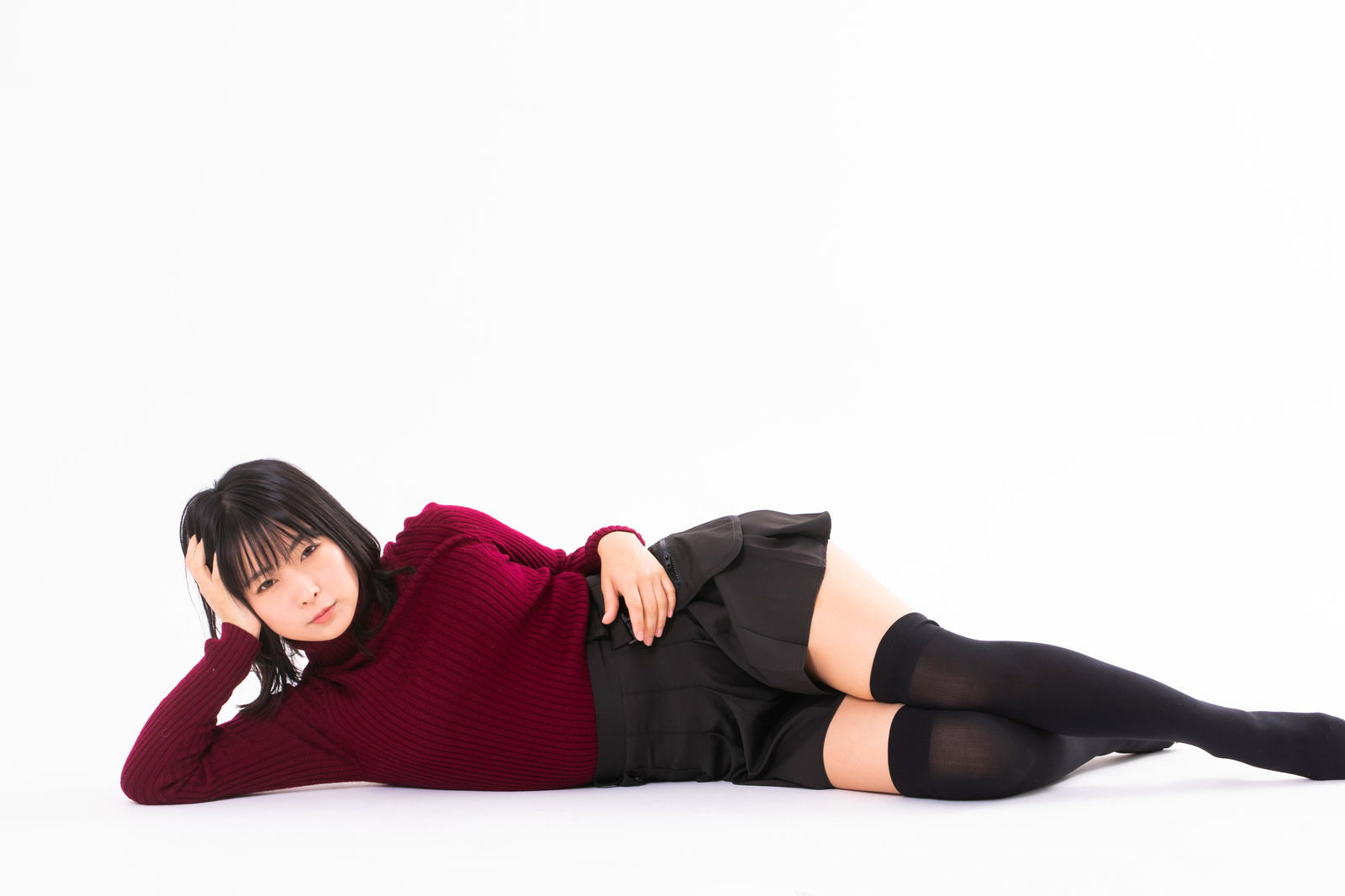 赤いトップスを着て横たわりながら肘枕をするモデル女性［モデル：にゃるる］