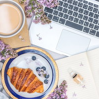 木製デスクに散らばる花とクロワッサンの朝食の写真