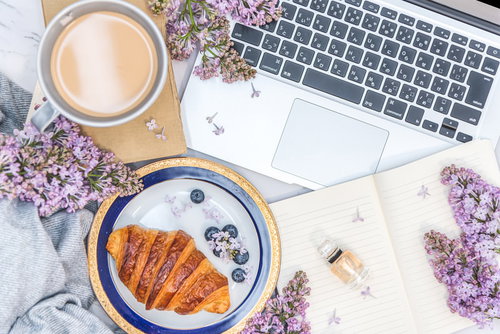 木製デスクに散らばる花とクロワッサンの朝食