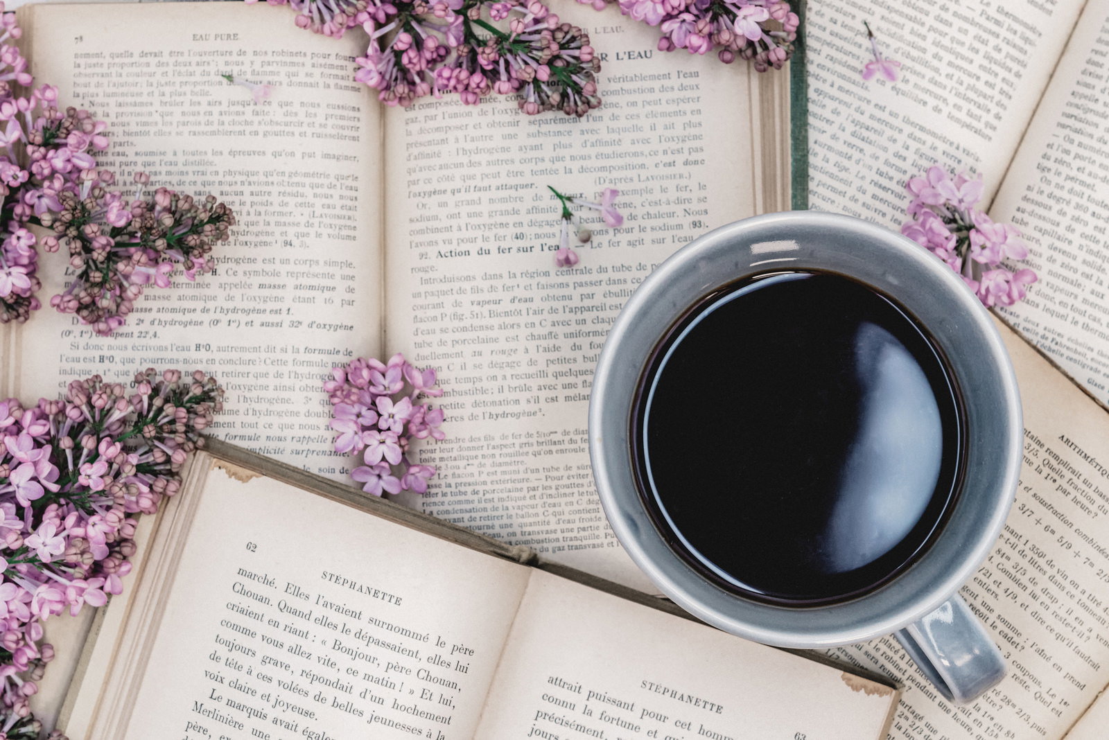 洋書に置かれたコーヒーカップとライラック