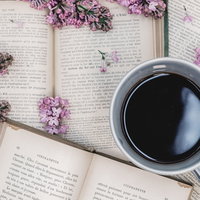 散らばる洋書の上に置かれた珈琲カップとライラックの写真