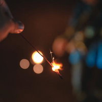 線香花火を持つ手と街明かりのぼかし、夏の夜のひとときの写真