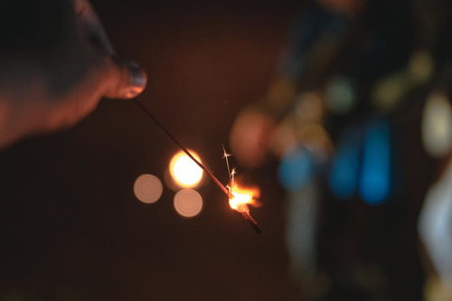 線香花火を持つ手と街明かりのぼかし、夏の夜のひととき