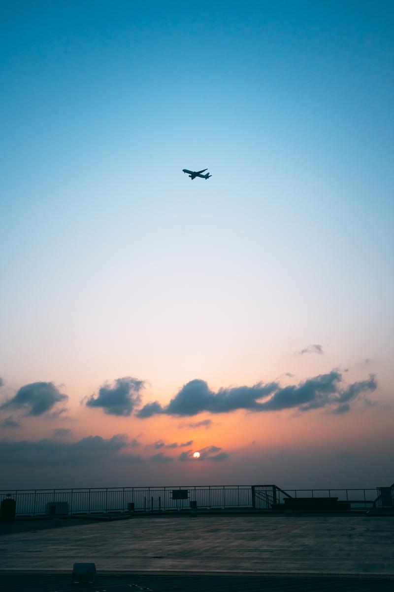 屋上から眺める夕焼け空を飛ぶ飛行機のシルエット