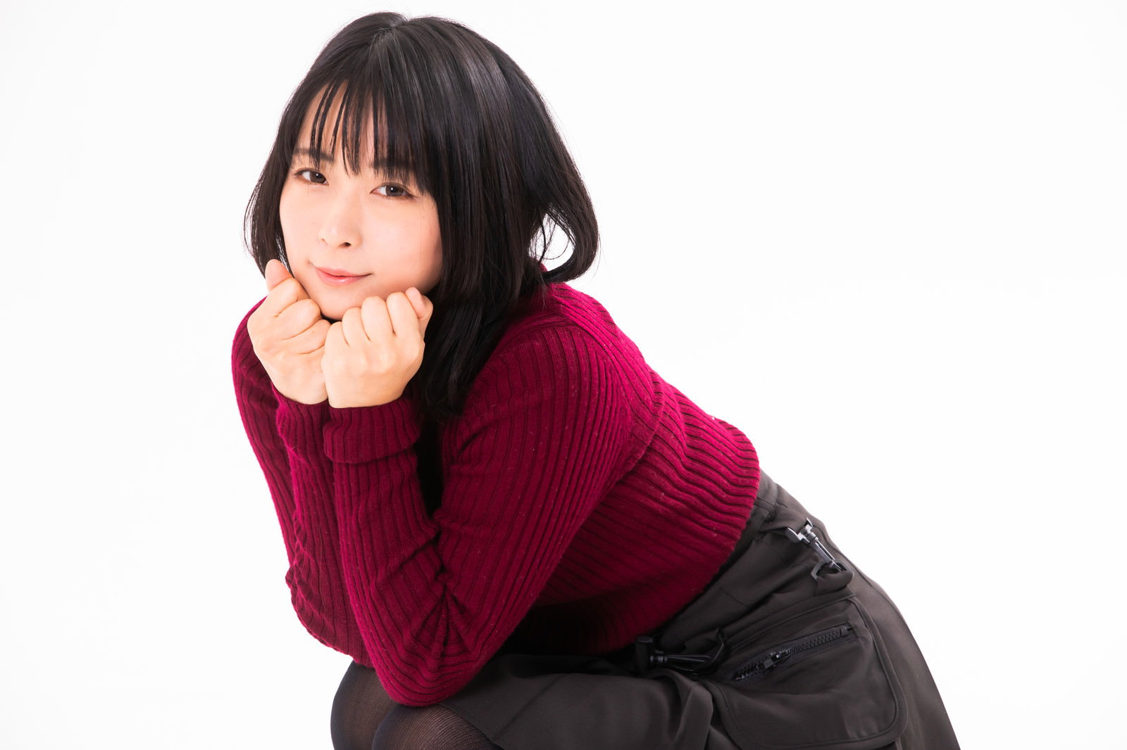 赤い服を着た女性が顎に手を添えて上目遣いで見つめるポーズ［モデル：にゃるる］