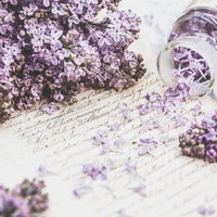 ガラス瓶からこぼれるライラックの花と手紙の写真