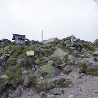 ガスで覆われた日光白根山山頂に建つ社と岩場の風景の写真
