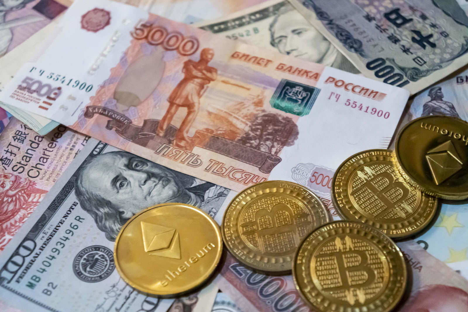 ロシアルーブル、米ドル、千円札などの紙幣とビットコイン、イーサリアムの暗号通貨コインが並んでいる様子