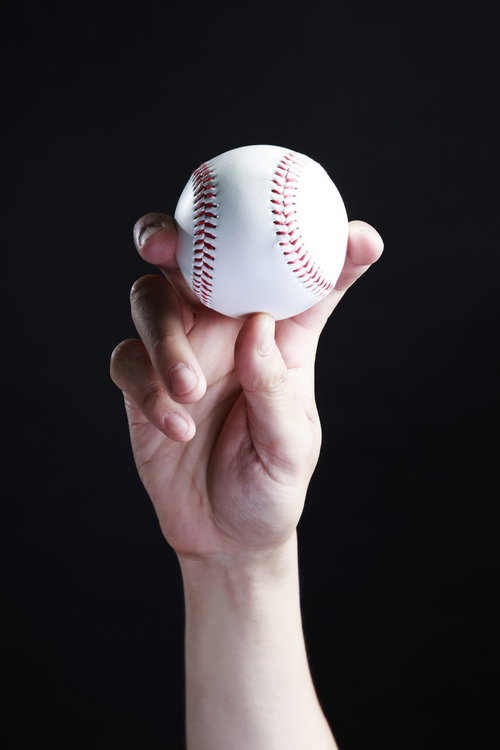 黒い背景でフォークボールを握る野球選手の投球フォーム