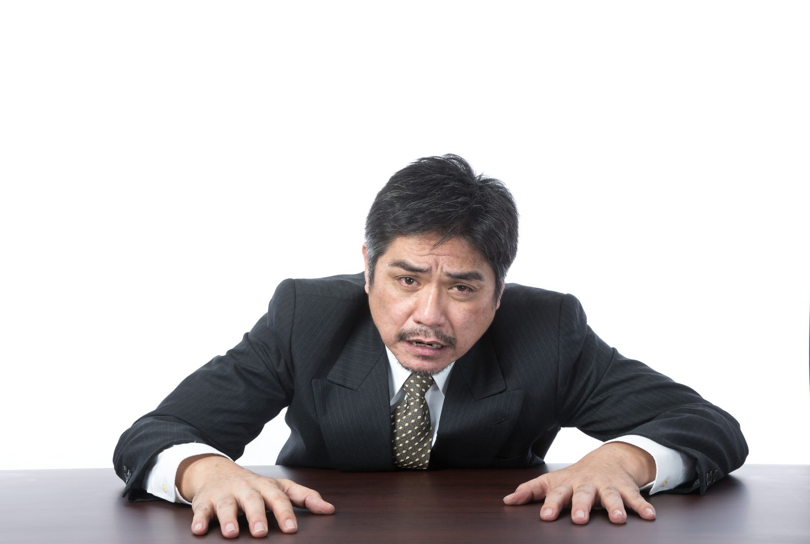 机に両手をついて苦しい表情の紺スーツ姿の男性［モデル：よたか］