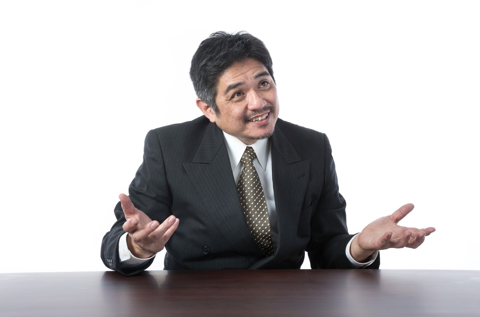 笑顔で両手を広げて説明するスーツ姿の中年男性［モデル：よたか］