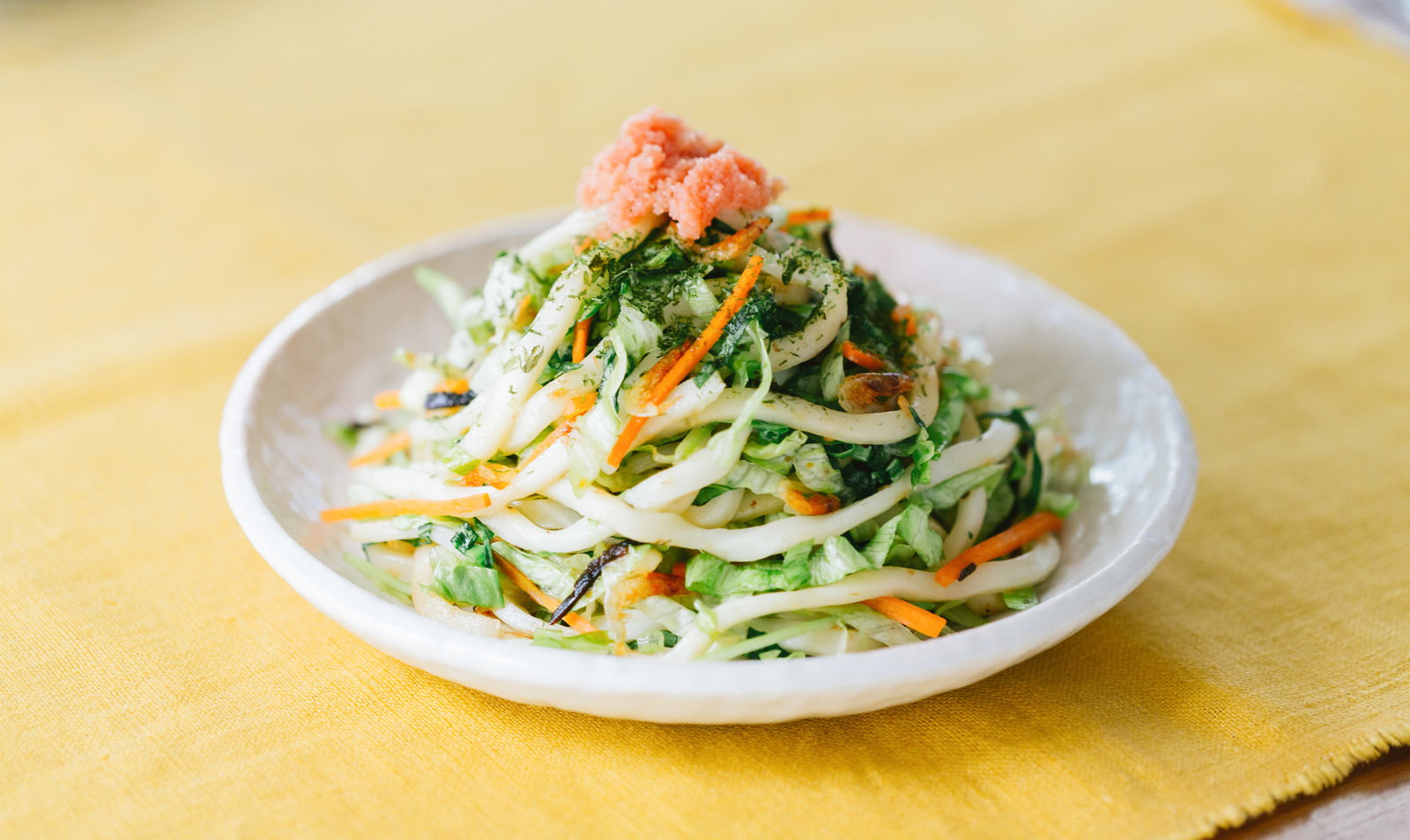 白い皿に盛り付けた焼きうどんに明太子をトッピング、白菜としらたきを混ぜたサラダを添えた低カロリー食