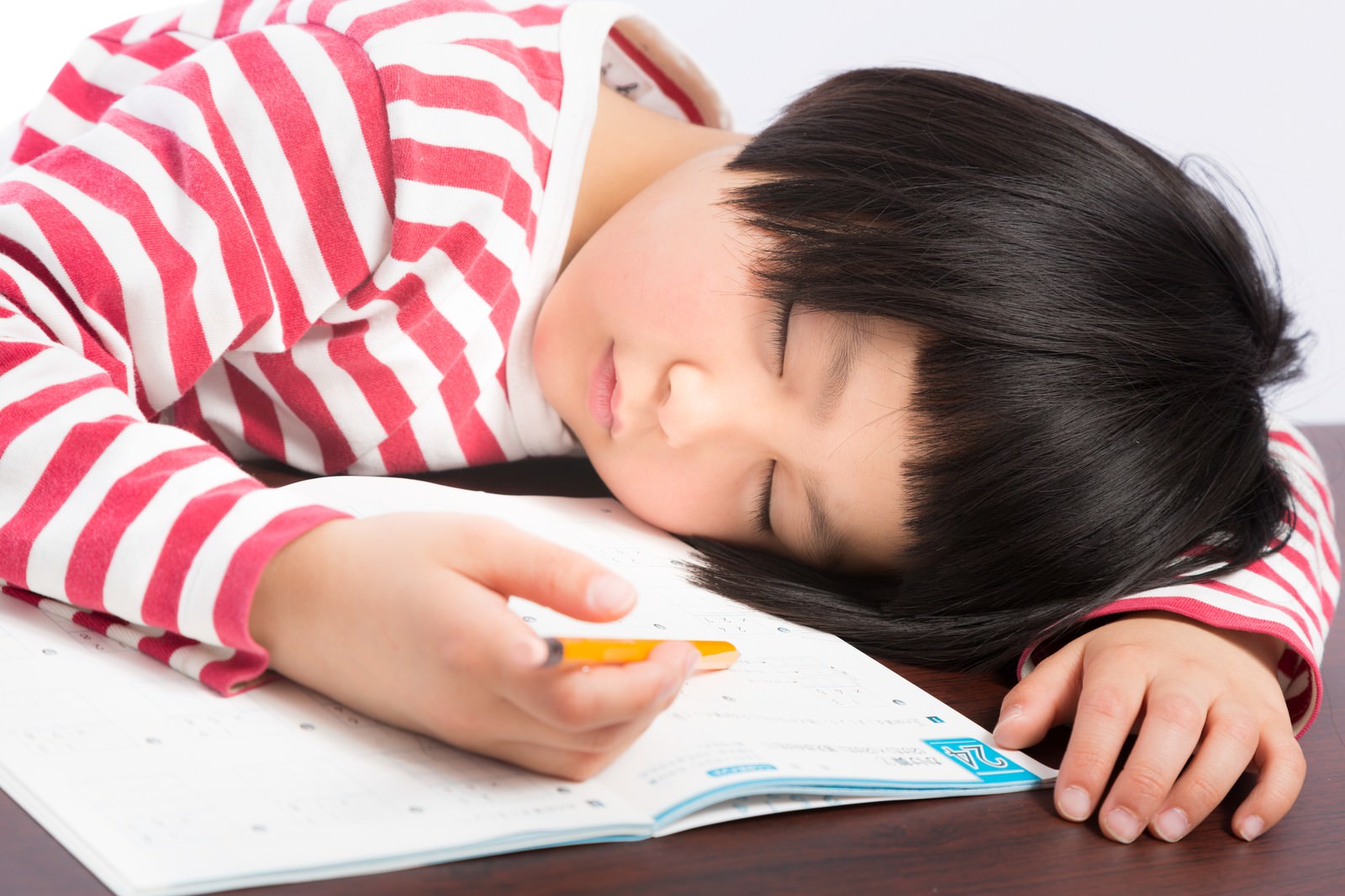 机に頭を乗せて寝ている、ピンクと白のボーダーシャツを着た前髪パッツンの女の子［モデル：ゆうき］