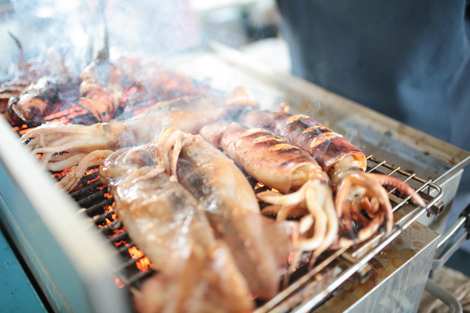 いすみ市の朝市で炭火焼きされた複数のイカが金属網に並んでいる様子