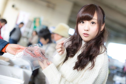 朝市で新鮮なタコを試食する白いニット姿の女性