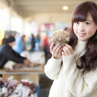 いすみ市の朝市でホタテをPRする女性レポーターの写真