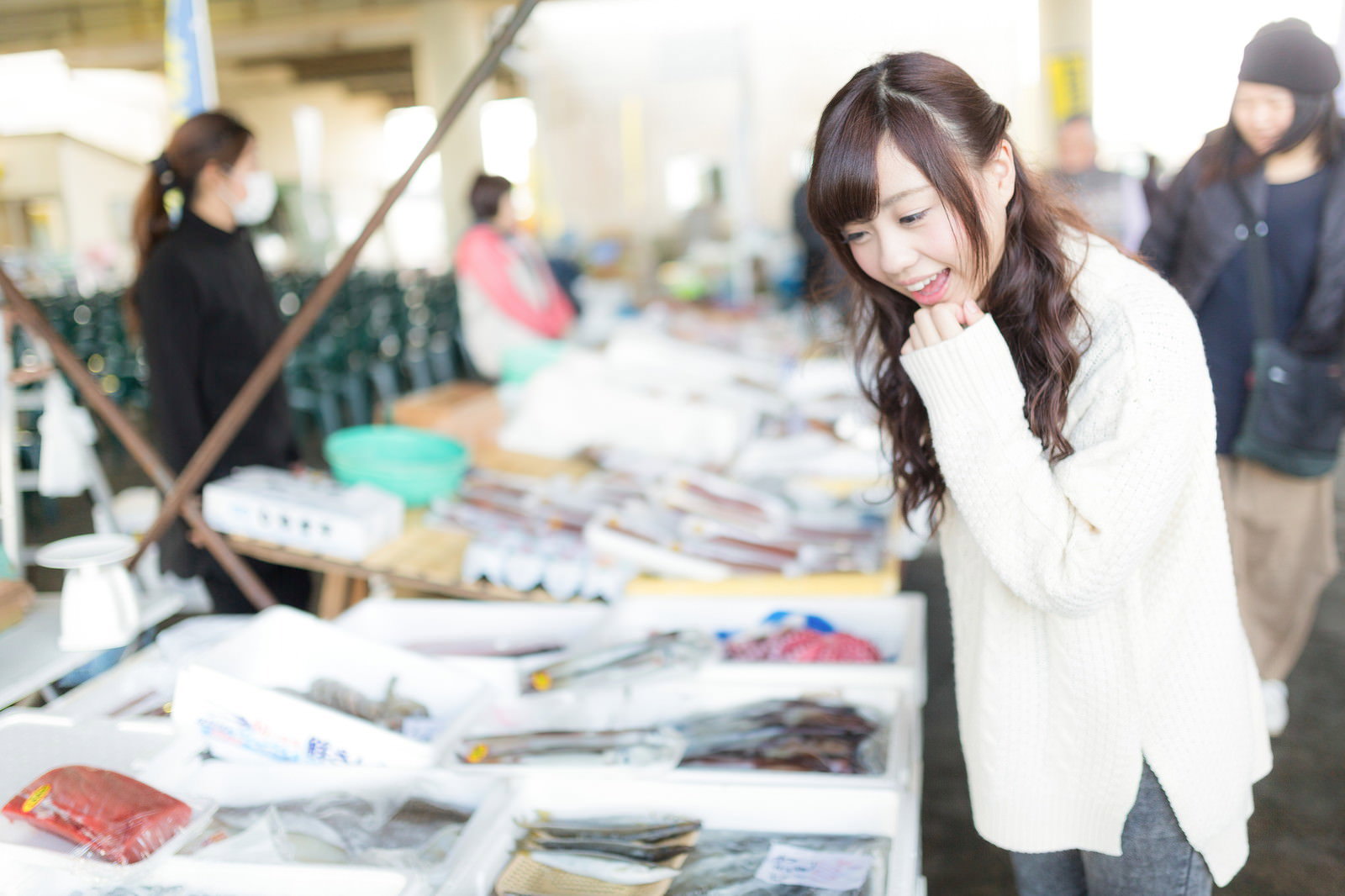 いすみ市の朝市で魚を見て吟味する白いセーター姿の女性［モデル：河村友歌］