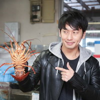 活きた伊勢海老を手に持ってアピールする男性の写真