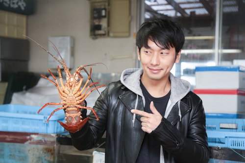 活きた伊勢海老を手に持ってアピールする男性の写真