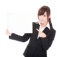 白いボードを持って指をさすビジネス女性の案内係の写真