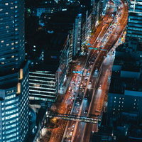 ビル群の間を通る幹線道路と車列が連なる夜間の都市風景の写真