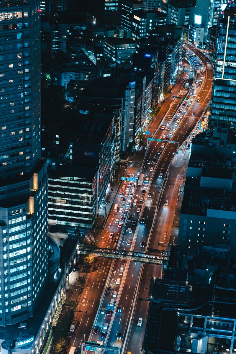 ビル群に囲まれた幹線道路を走る車列の夜景