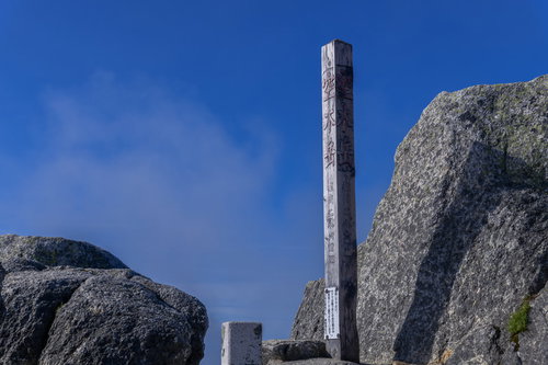 快晴の空の下、中央アルプスの空木岳山頂に立つ白い山頂碑