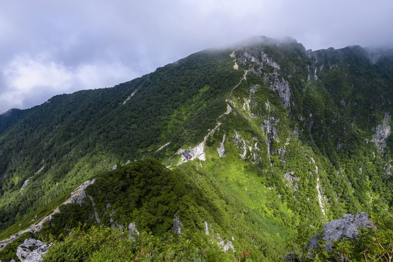 緑の山々に囲まれた谷間に建つ木曽殿山荘と雲がかかる空木岳の風景