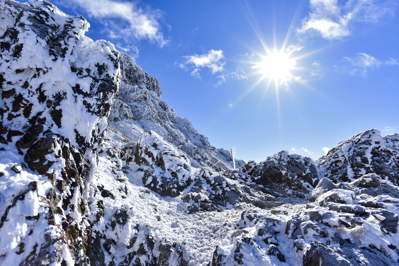 雪に覆われた赤岳の険しい斜面と青空に輝く太陽が写る快晴の山岳風景