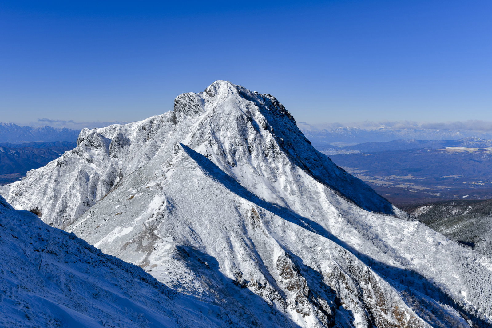 快晴の青空の下、雪化粧した阿弥陀岳の山頂部
